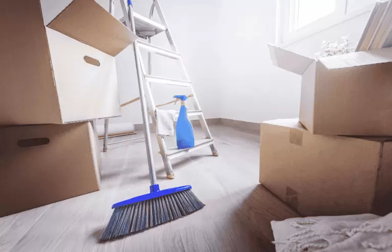 Broom and cleaning bottle next to moving boxes